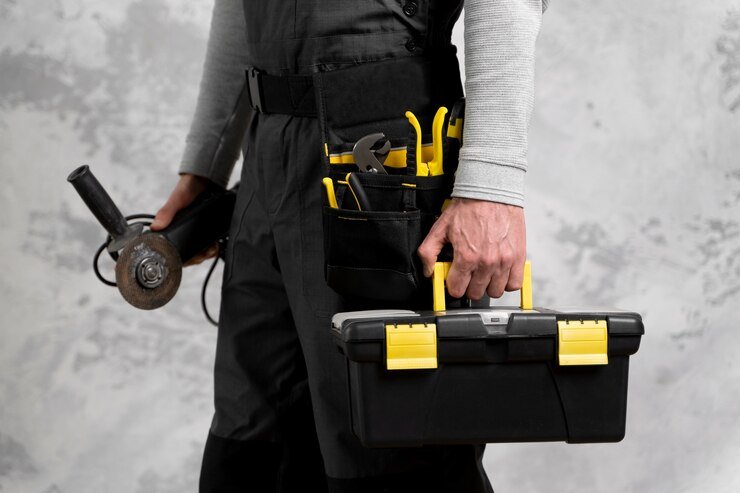 A man in overalls holding a toolbox.